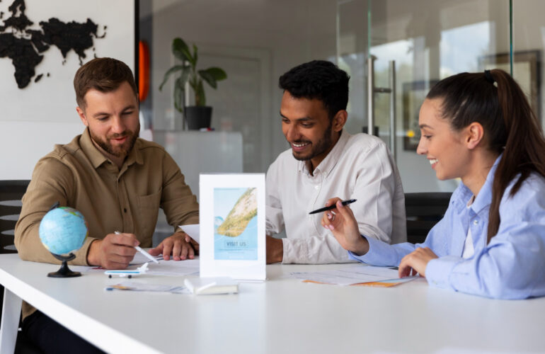 Three professionals discussing job opportunities around a table with a globe and travel brochures in the background, representing Work Abroad Agencies